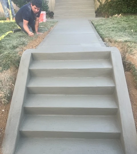 A man is kneeling down next to a set of concrete stairs.