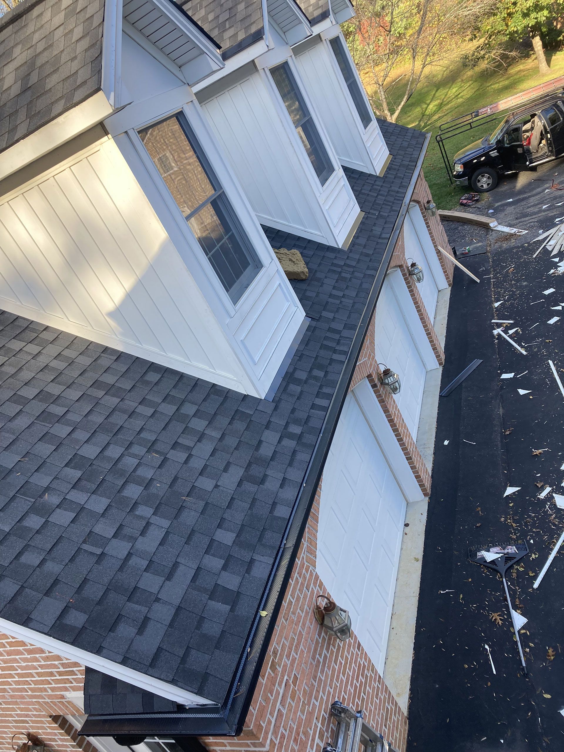 Roof of a two-story brick home with dark gray shingles, dormer windows, and a driveway.