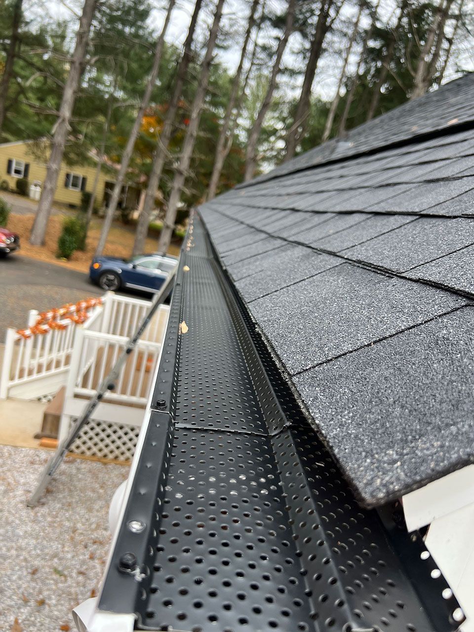 Close-up view of a house roof with black gutter guards. Trees and other houses are in the background.