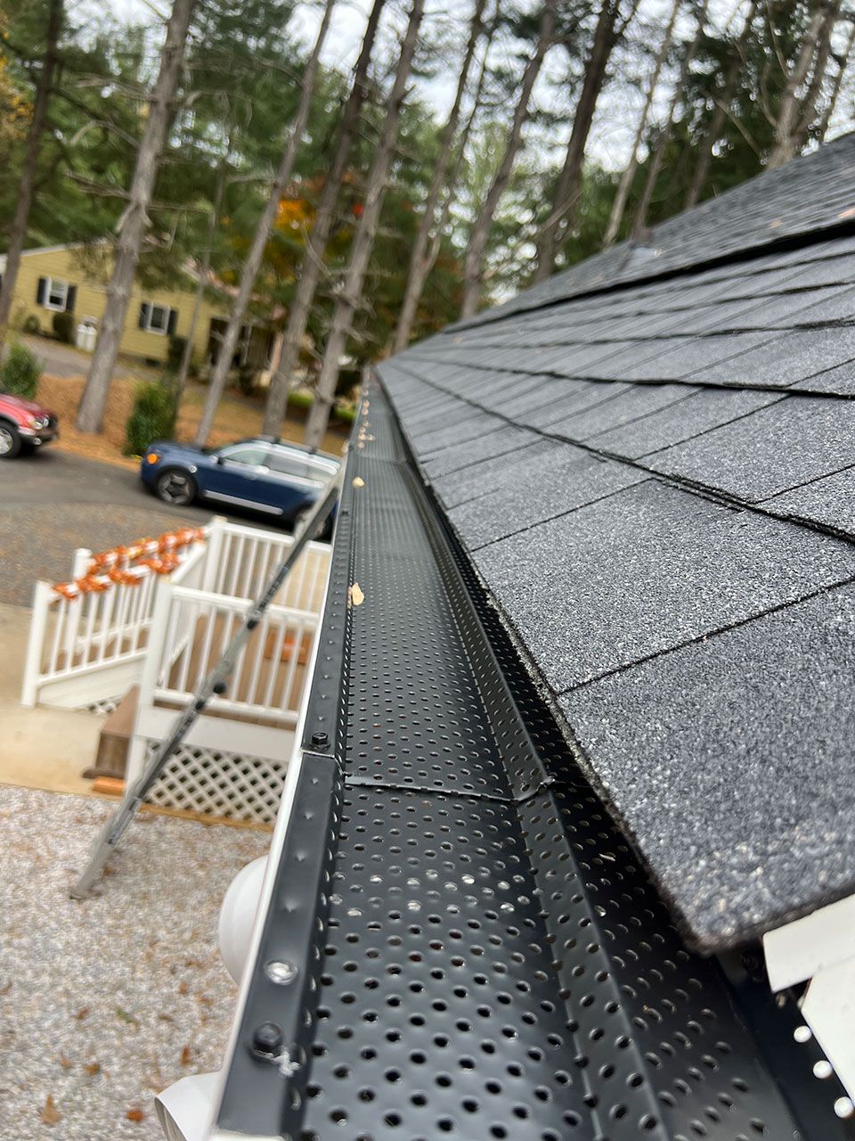 Black gutter with mesh cover installed on a roof with dark shingles, near a white deck and trees.