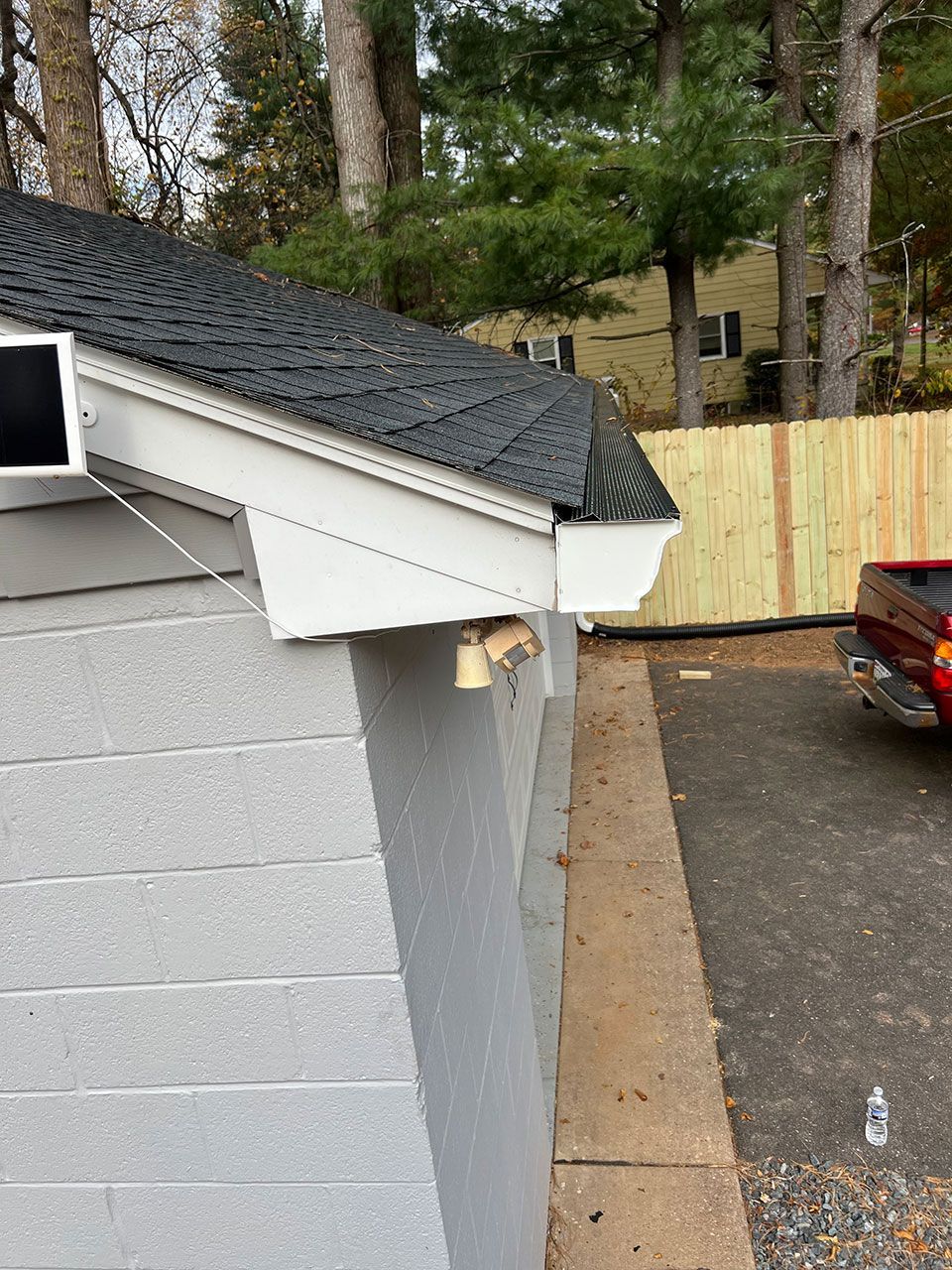 Side view of a building with a black shingled roof, light gray walls, and a white overhang.