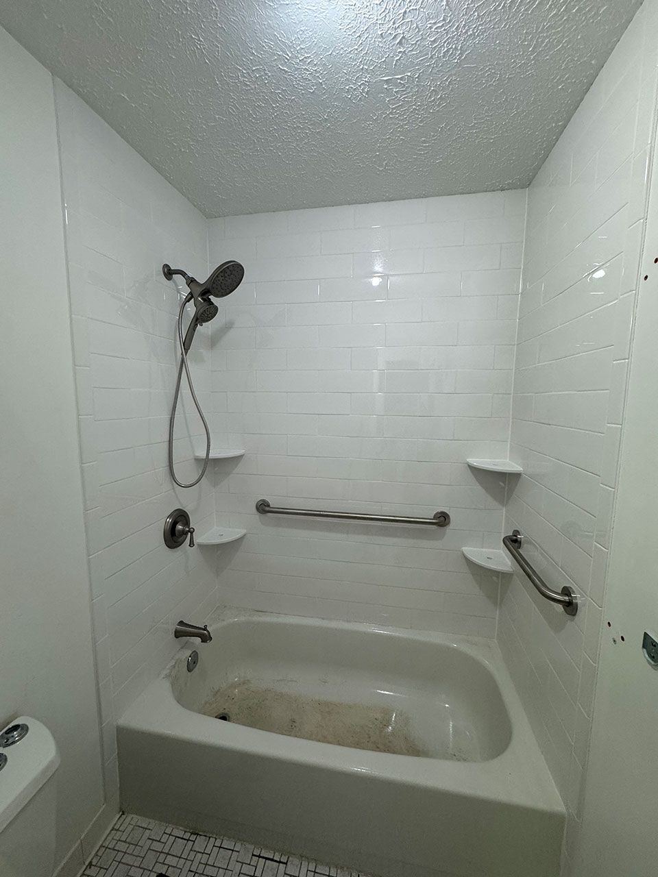 White bathroom with bathtub, showerhead, grab bars, and shelves.