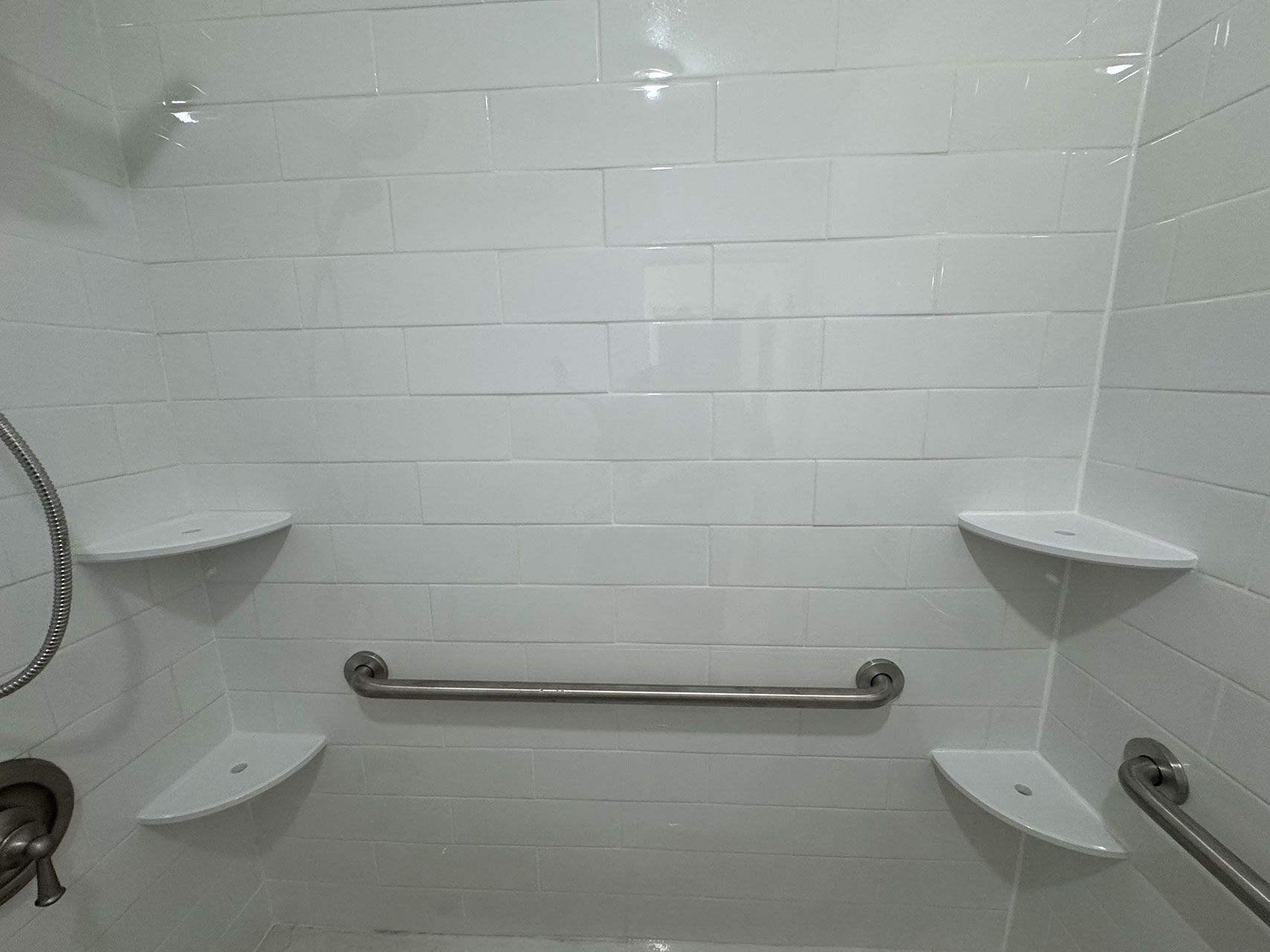 White-tiled shower with three corner shelves, a grab bar, and a showerhead.
