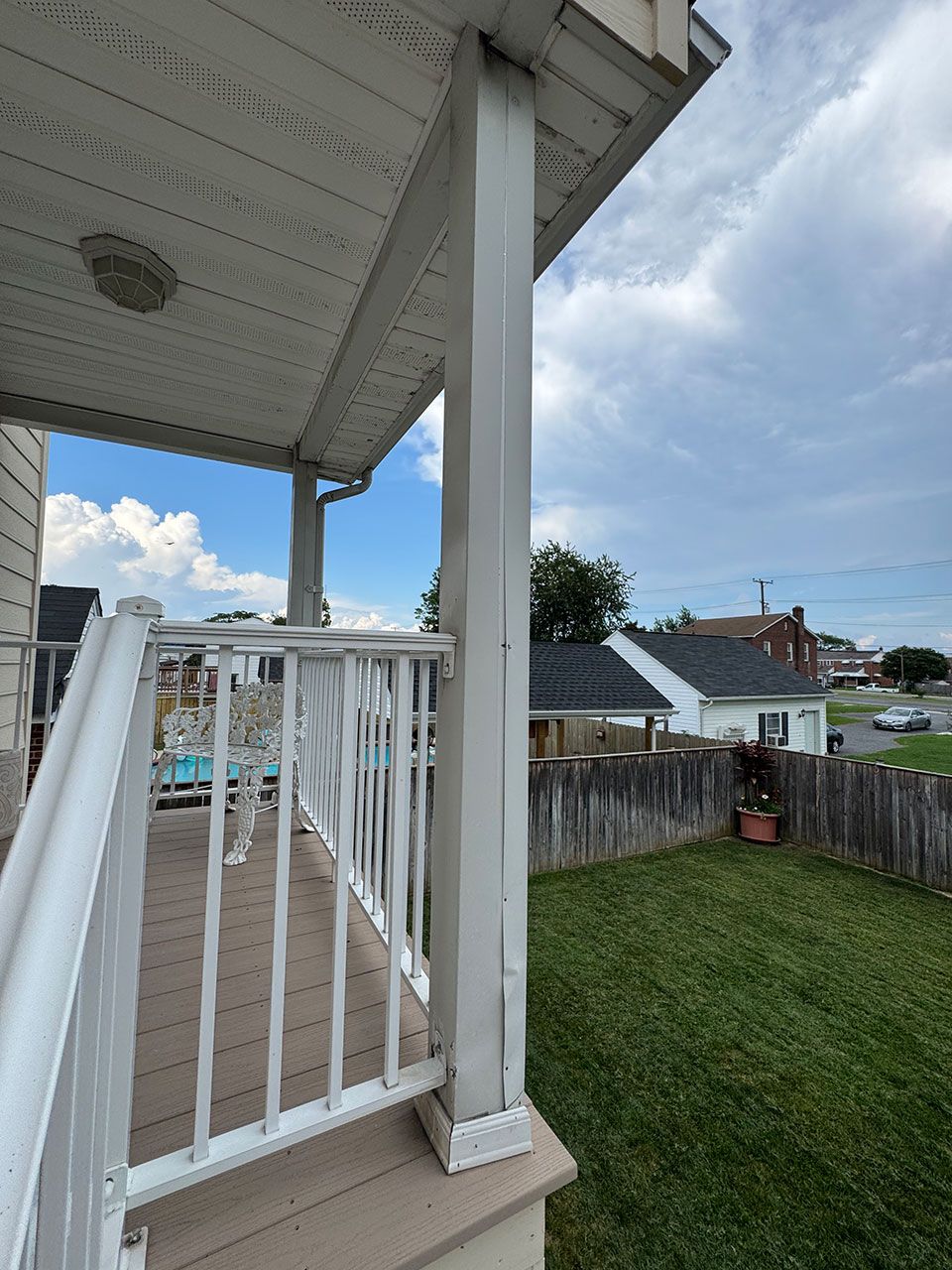 White porch with railing, post, and composite decking. Green lawn, blue sky, and houses in the background.