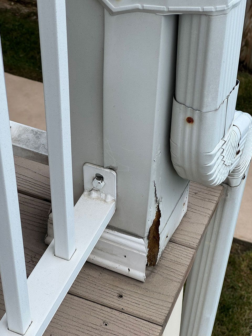 White deck post with railing and gutter, damaged and weathered.