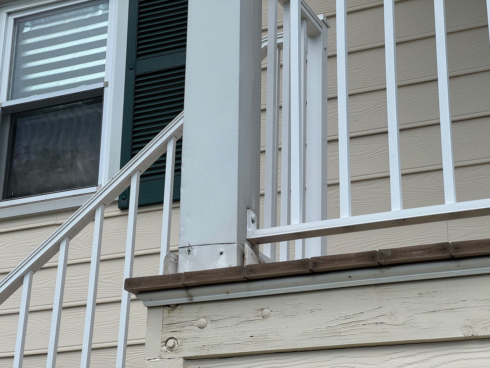 White porch railing and column, next to window with green shutters.