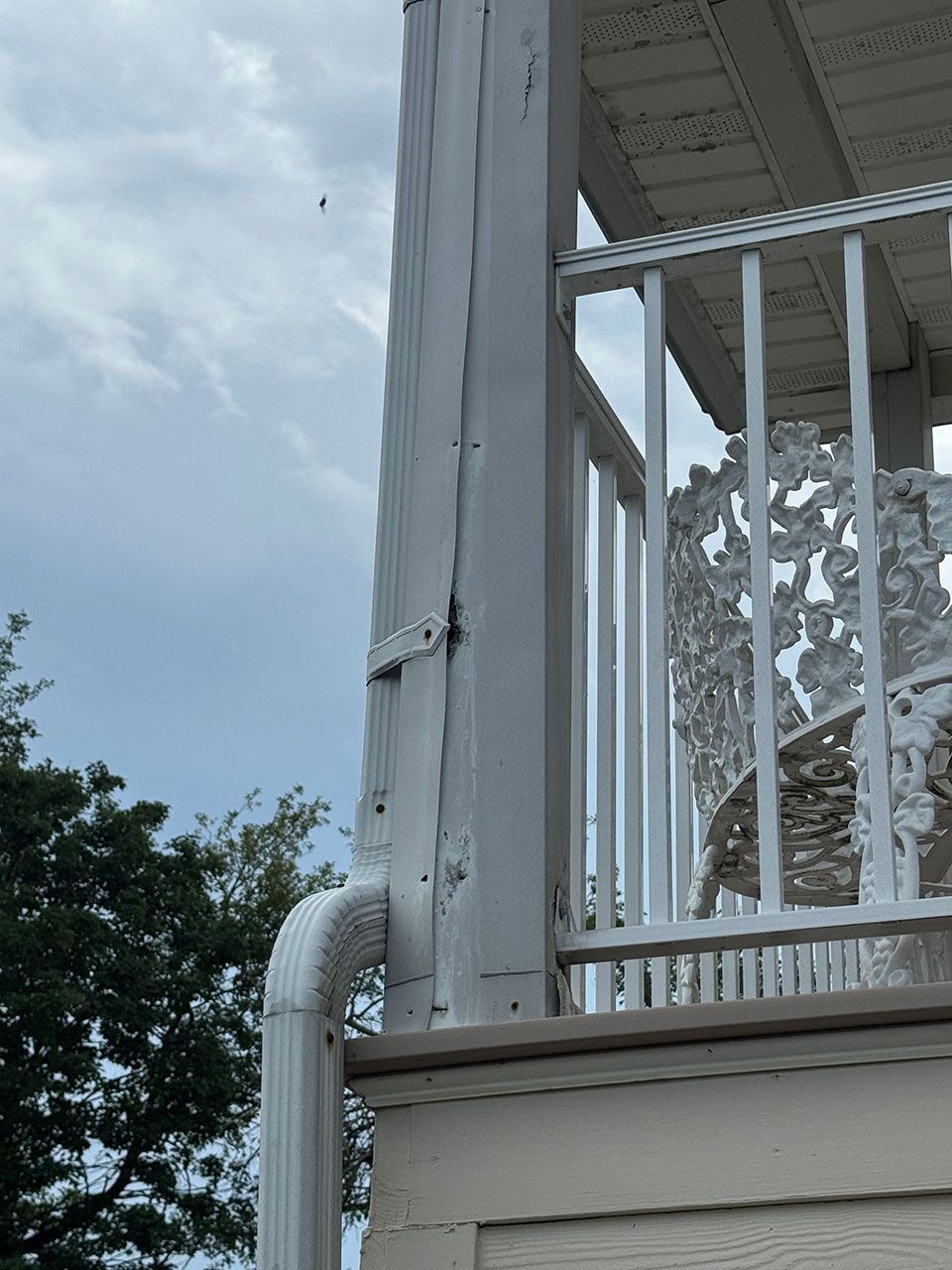 White painted deck support post with gutter. White railing and chair visible. Overcast sky in background.