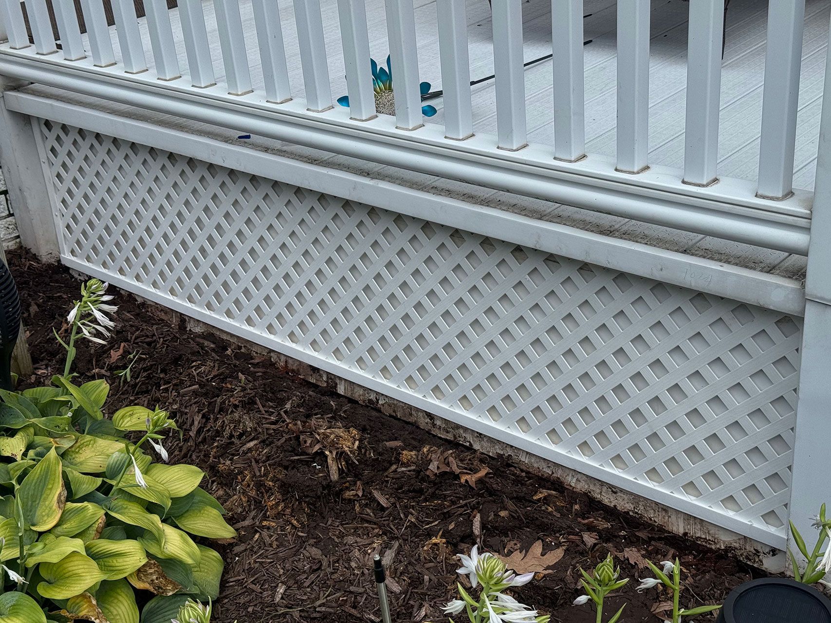 White lattice skirt of a deck, with railing above, next to a flower bed.