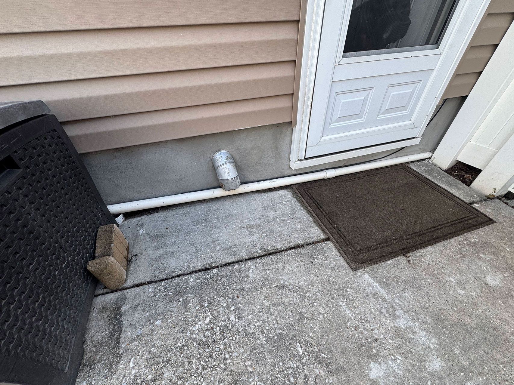 Exterior view of a door and porch. Door is white. A doormat is on the concrete. Beige siding is on the wall.
