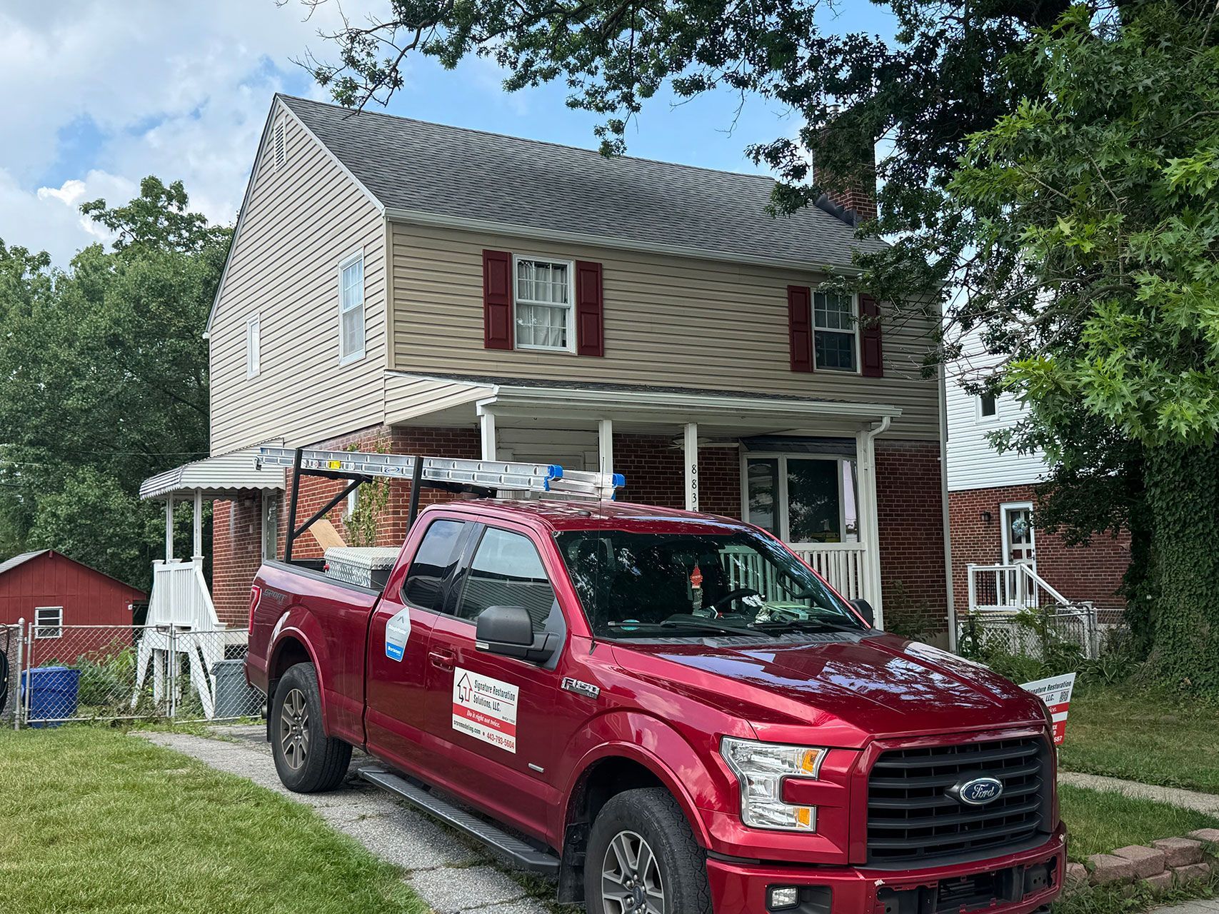 Red truck parked in front of two-story house with tan siding and red shutters.