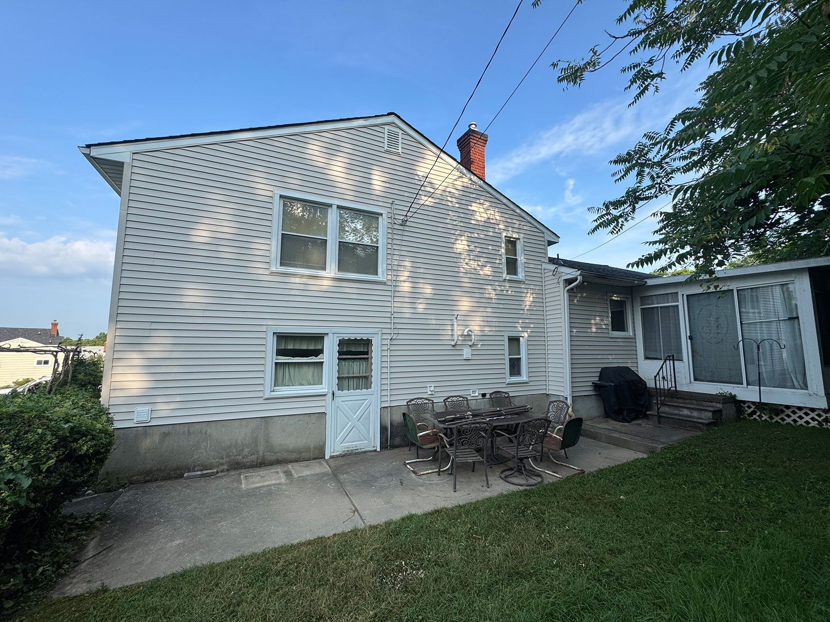Back of a two-story house with siding, patio, and grass. Features a chimney and a small shed.