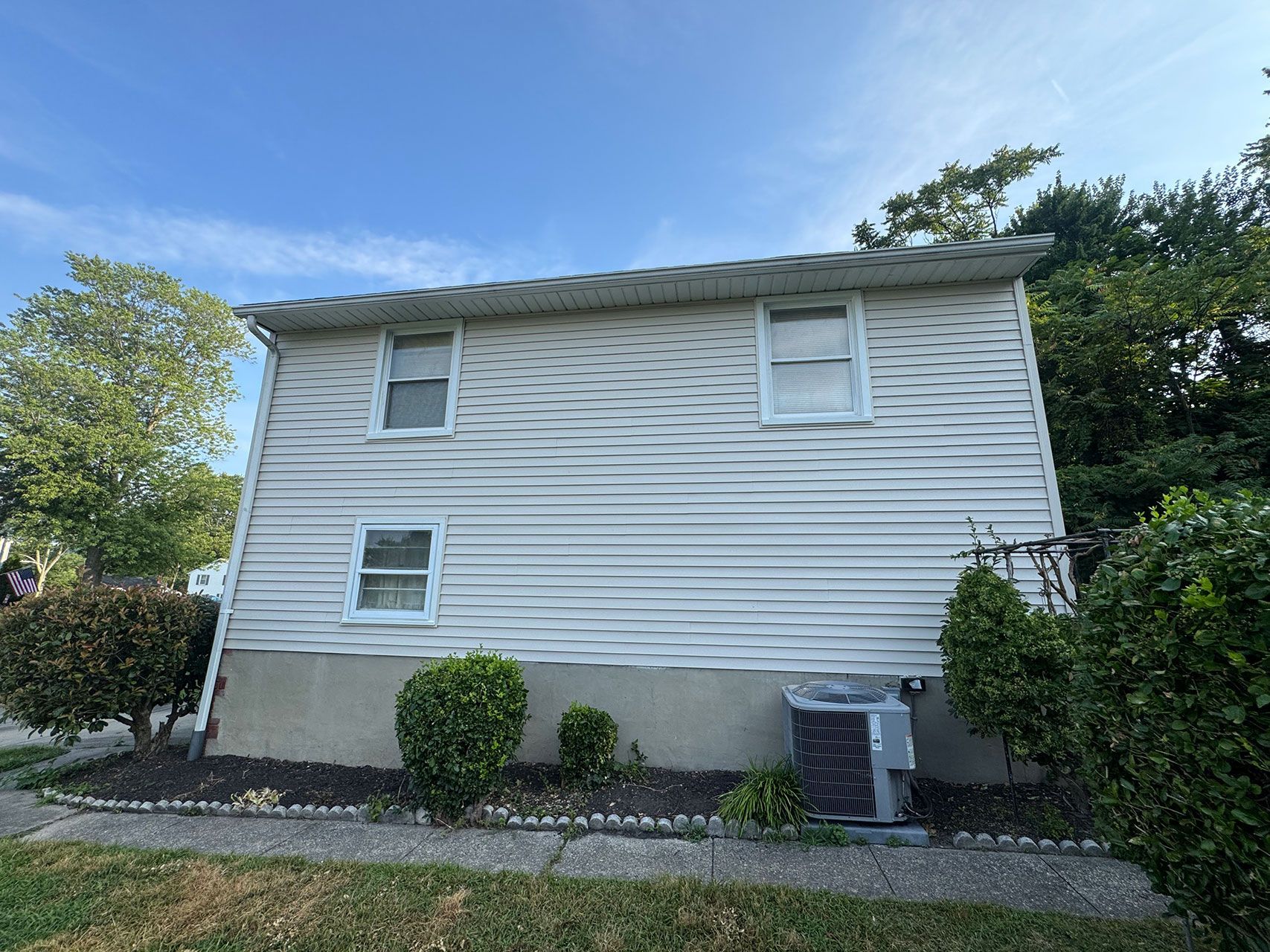 Side view of a two-story white house with windows and an air conditioning unit; blue sky.