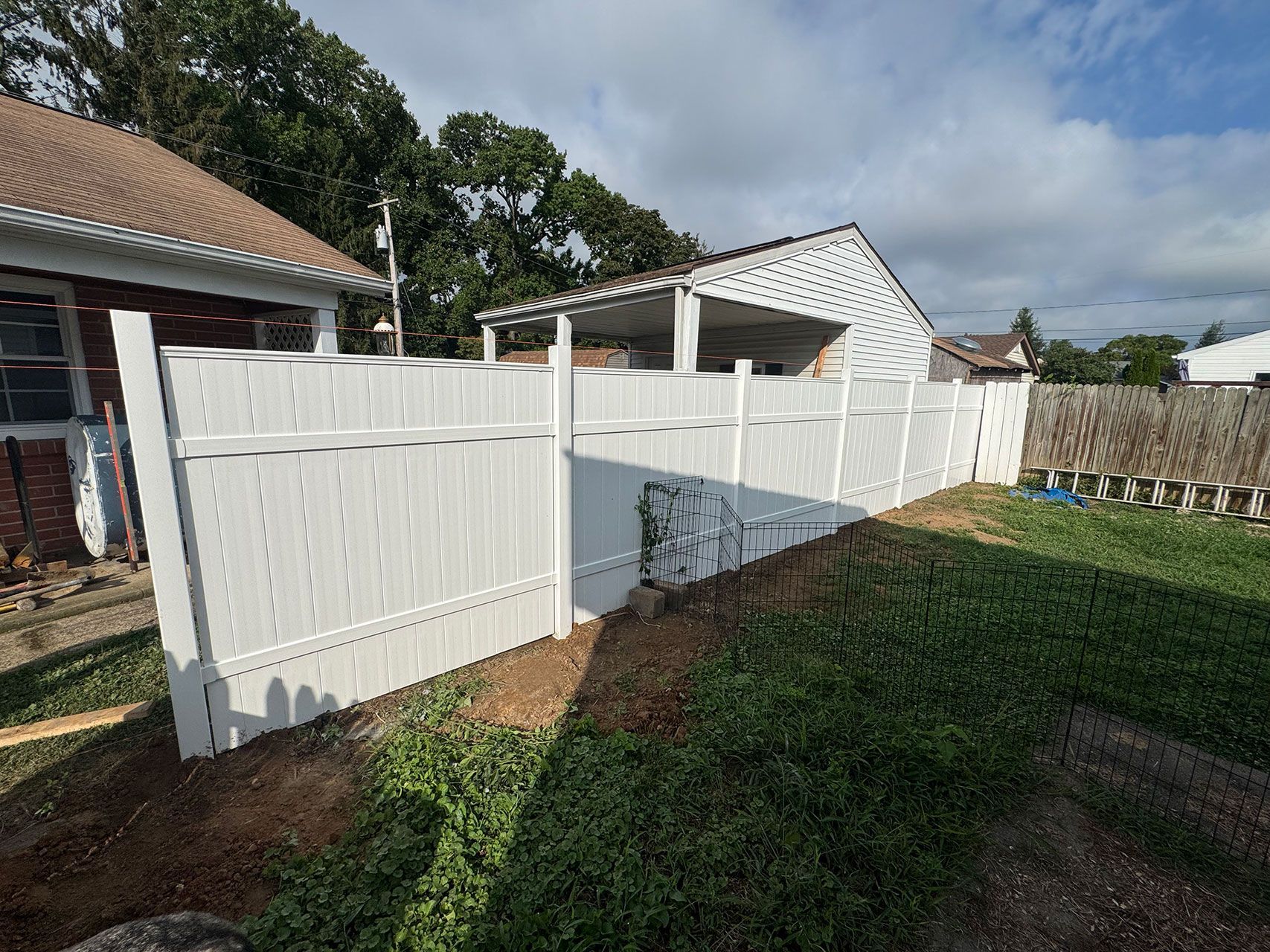 White vinyl fence in a backyard setting, next to a brick house and green grass.