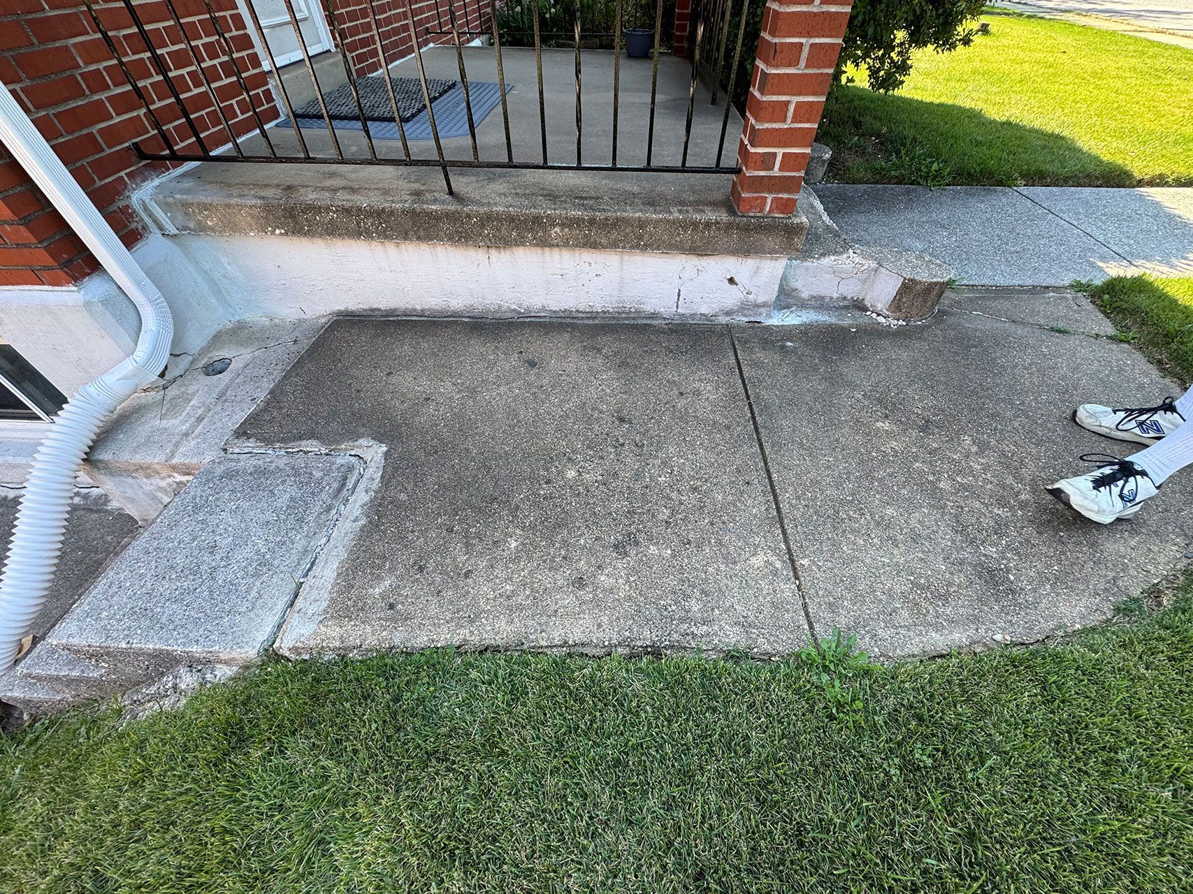 Concrete front steps with damage, next to a grassy lawn and brick house.