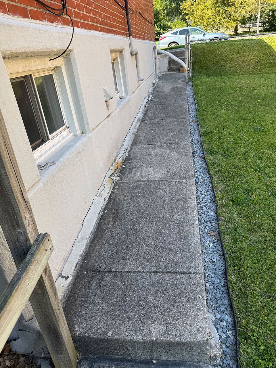 Concrete walkway alongside a building's foundation, bordered by gravel and grass.