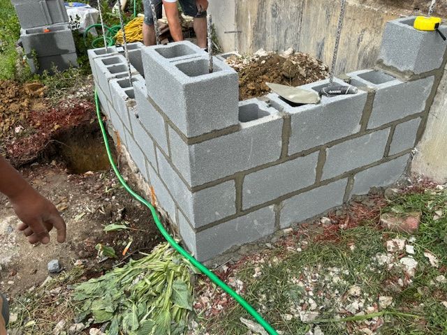 A person is working on a brick wall with a green hose attached to it.