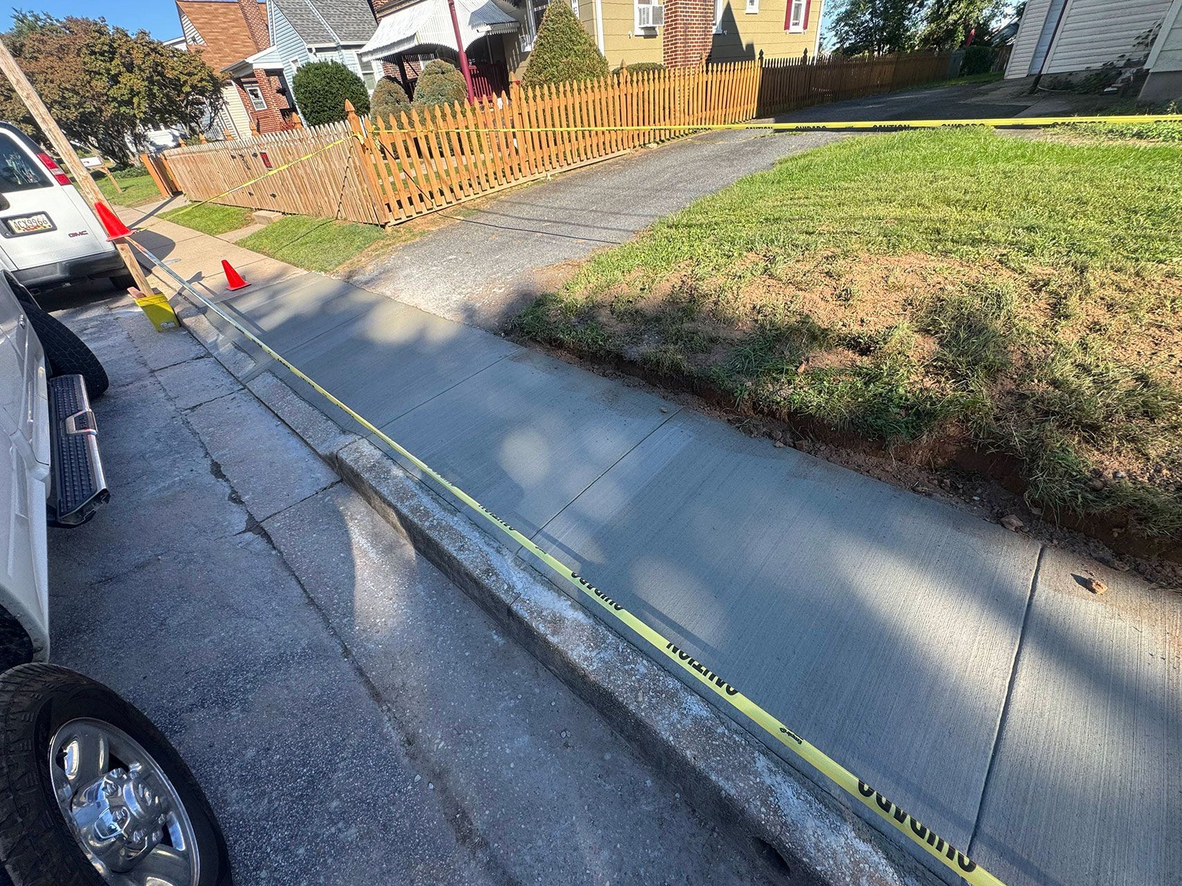 Freshly poured concrete sidewalk with caution tape and parked vehicles.
