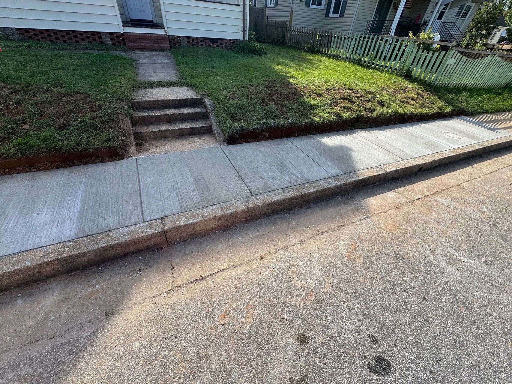 Sidewalk next to a road, leading to a house with grass and steps.
