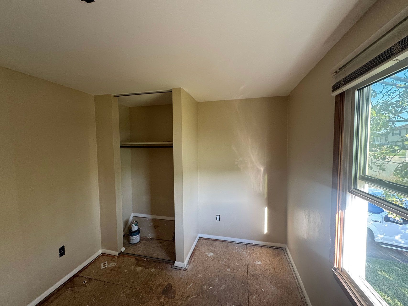 Empty bedroom with a built-in closet, unfinished floor, and a window letting in light.