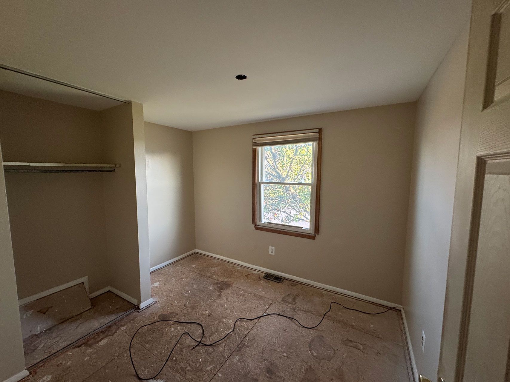 Empty room with a window and a closet, tan walls and a damaged floor.