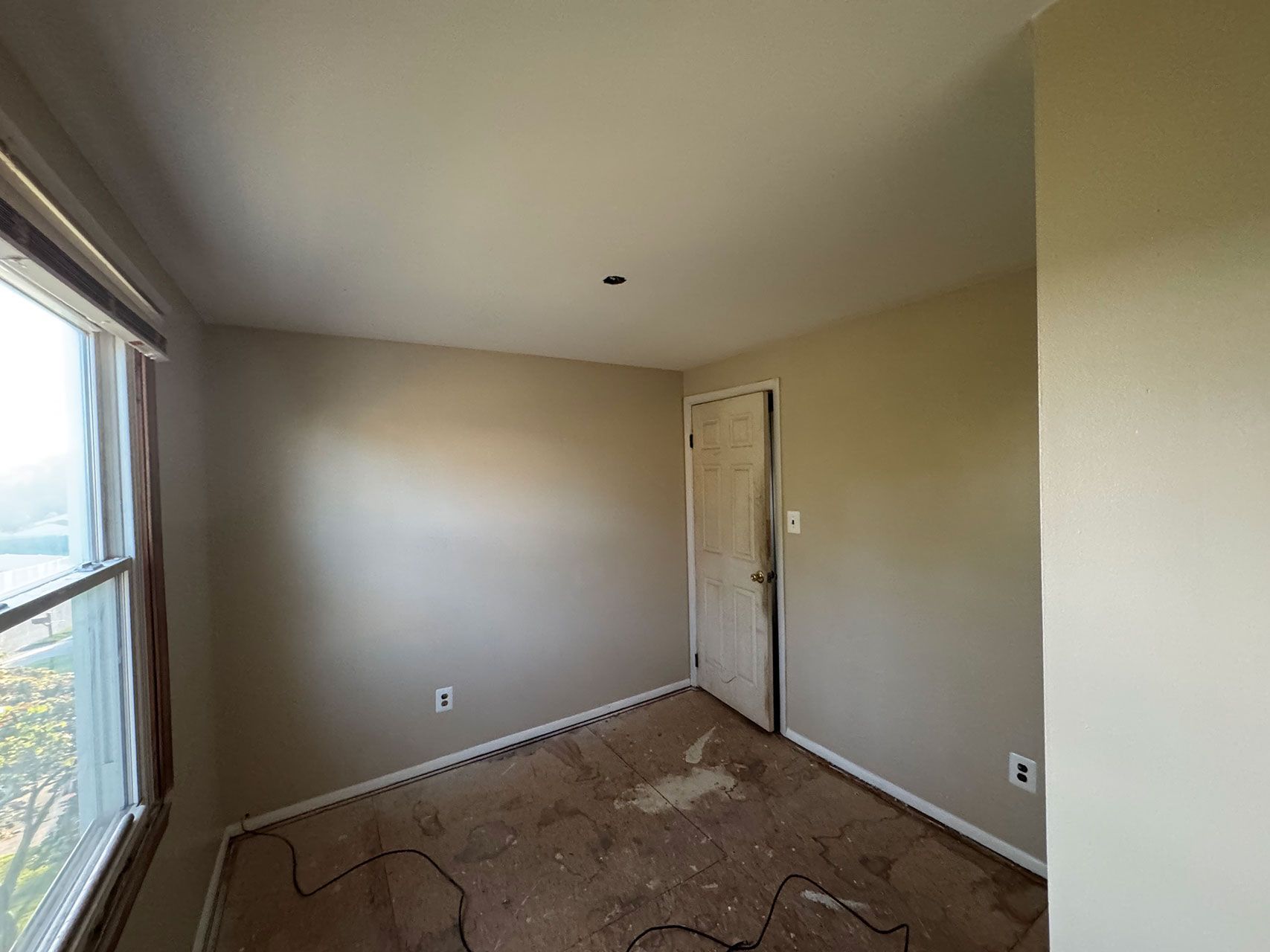 Empty room with a window, doorway, and damaged carpet. Beige walls and white ceiling.