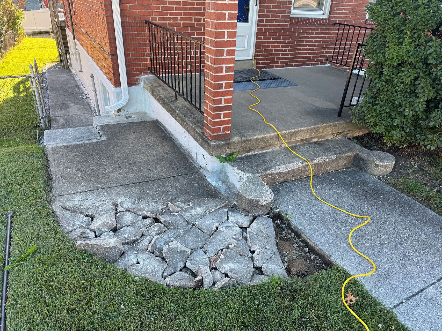 Damaged concrete sidewalk and steps leading to a brick building's porch, with a yellow cord running across the steps.
