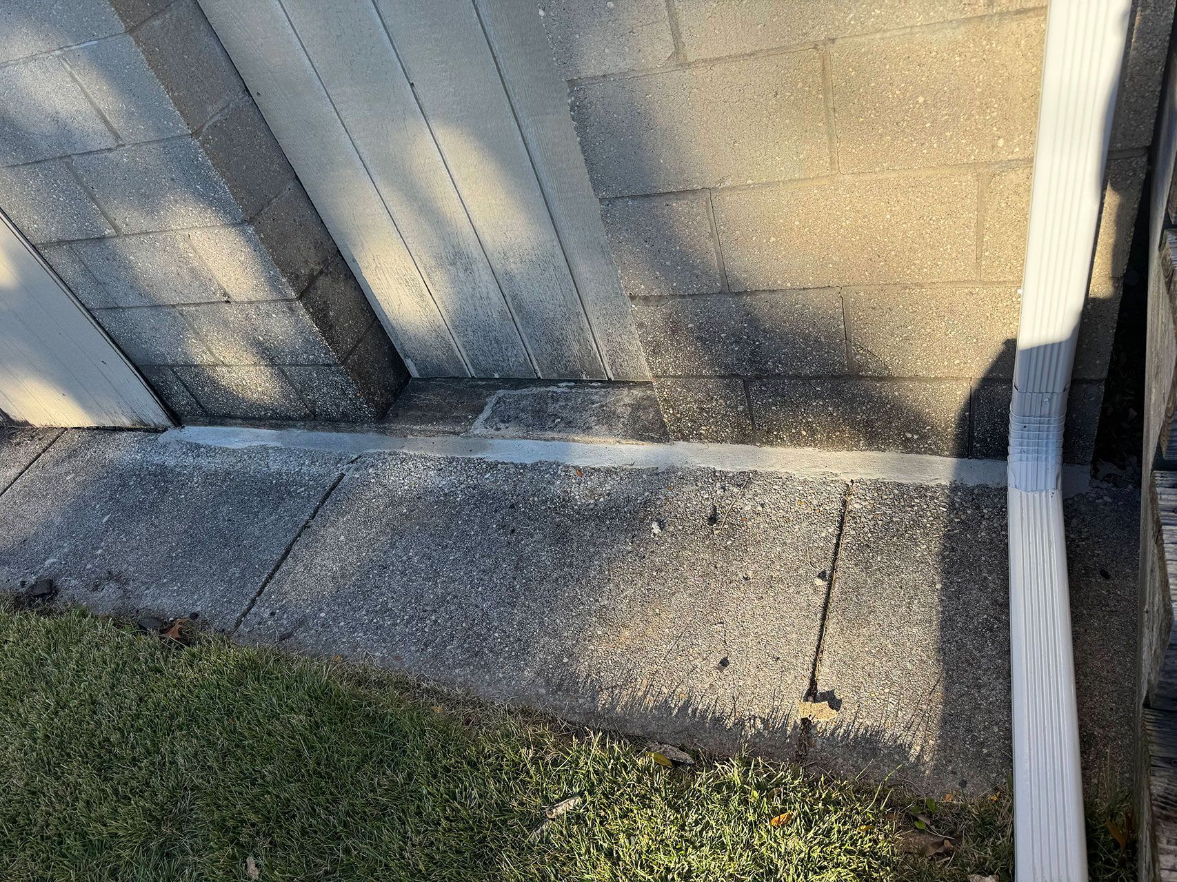 Roof edge with shingles and a gutter next to a grassy lawn.
