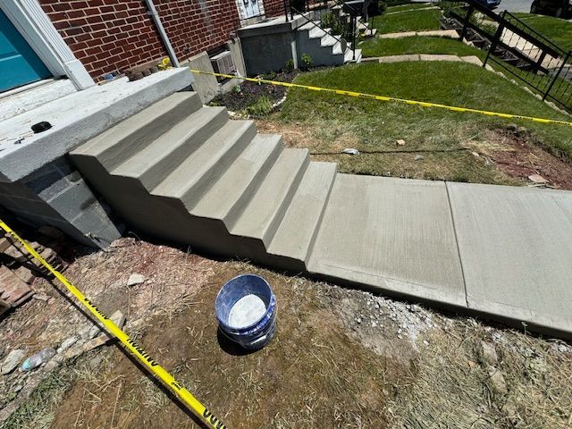 A bucket of concrete is sitting on the ground next to a set of stairs.