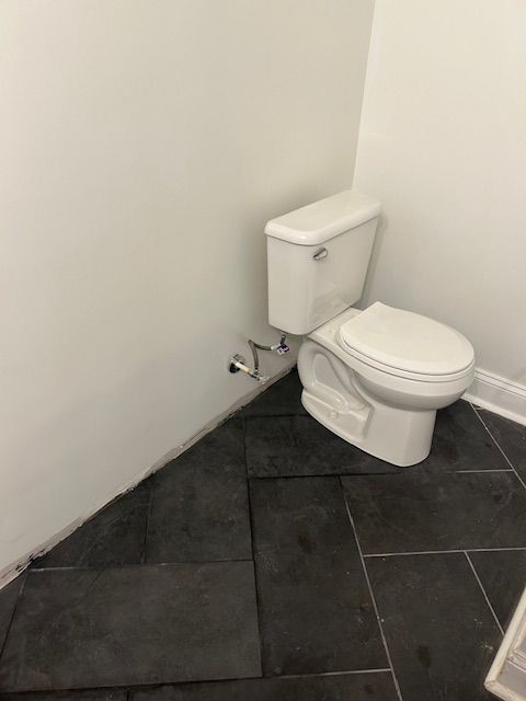 A toilet is sitting on a tiled floor in a bathroom.