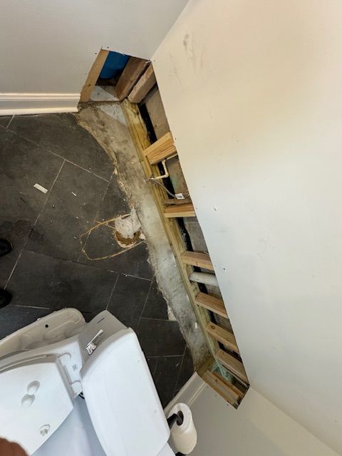 A toilet in a bathroom with a hole in the wall