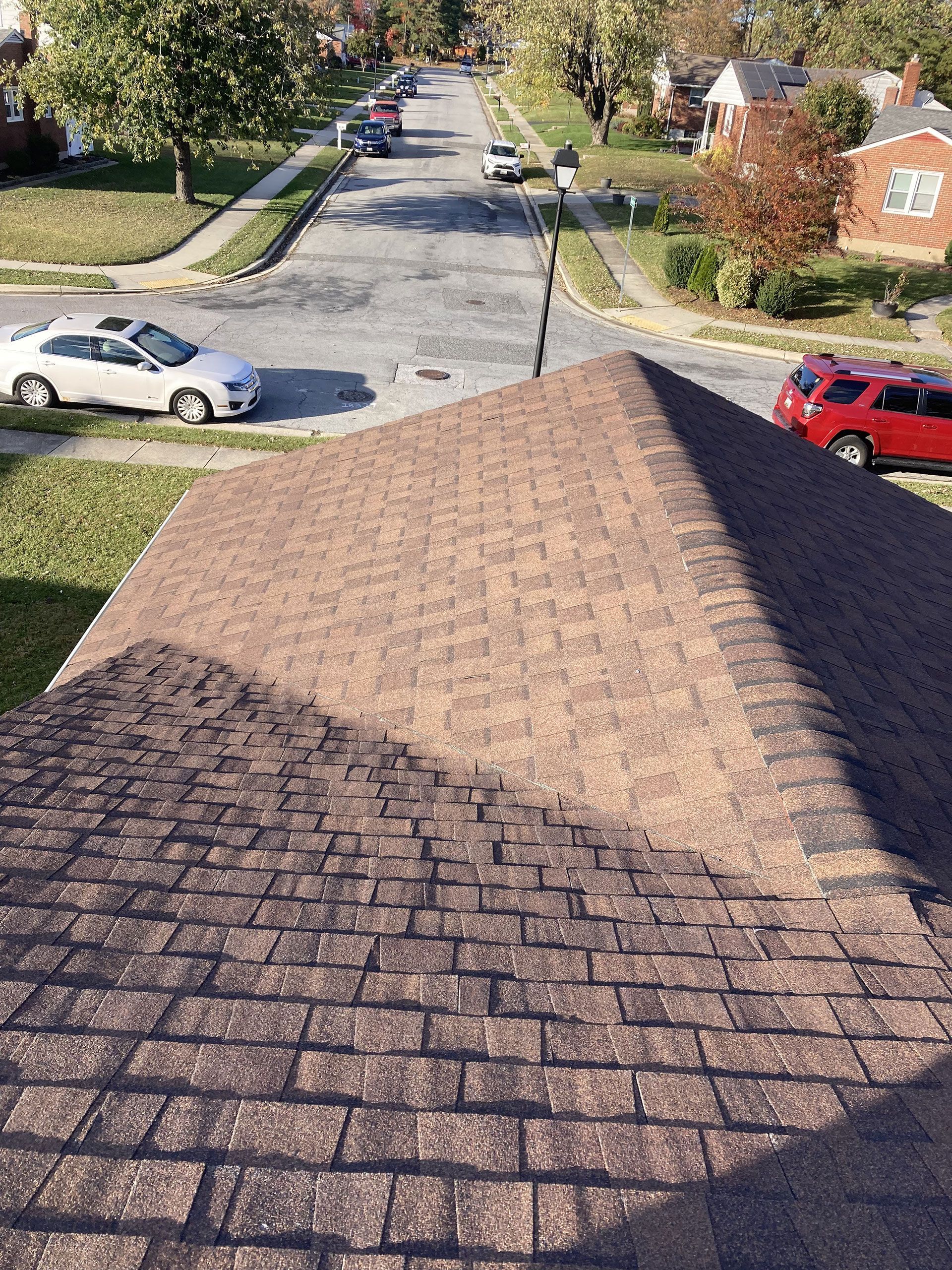 Brown shingle roof with a street and parked cars in the background on a sunny day.