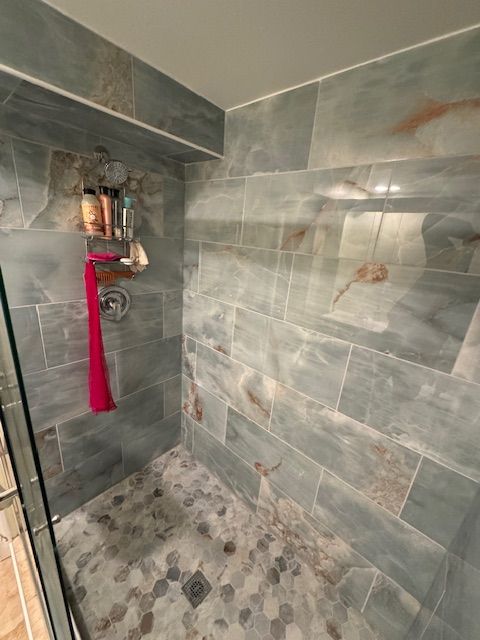 A walk in shower with a glass door and tiled walls.