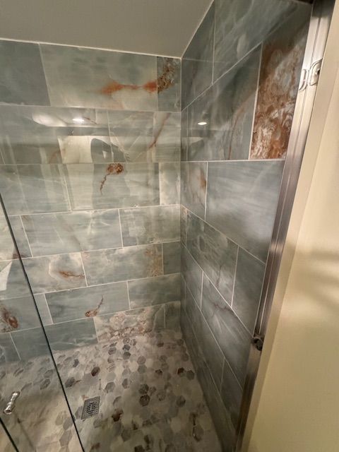 A walk in shower with a glass door and tiled walls.