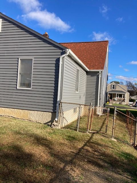 A gray house with a red roof and a fence in front of it.