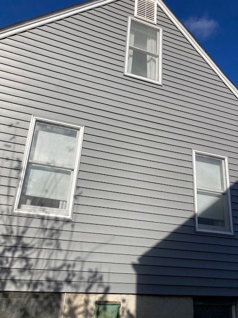 A gray house with white windows and a blue sky in the background.