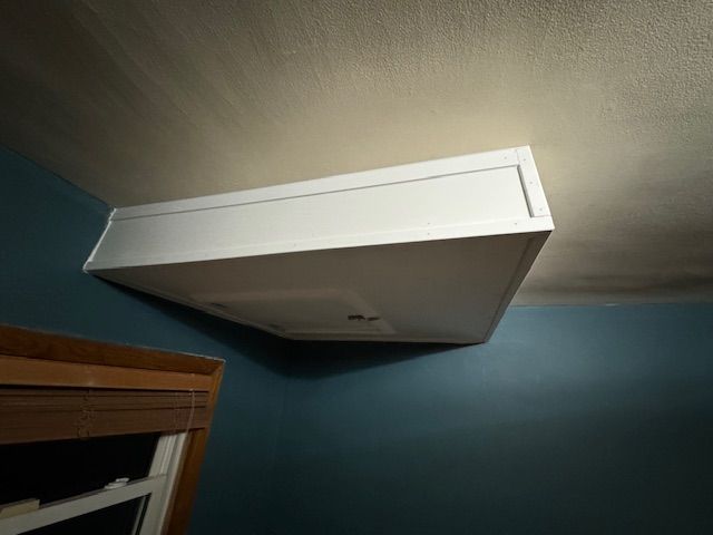 A white box is hanging from the ceiling of a room next to a window