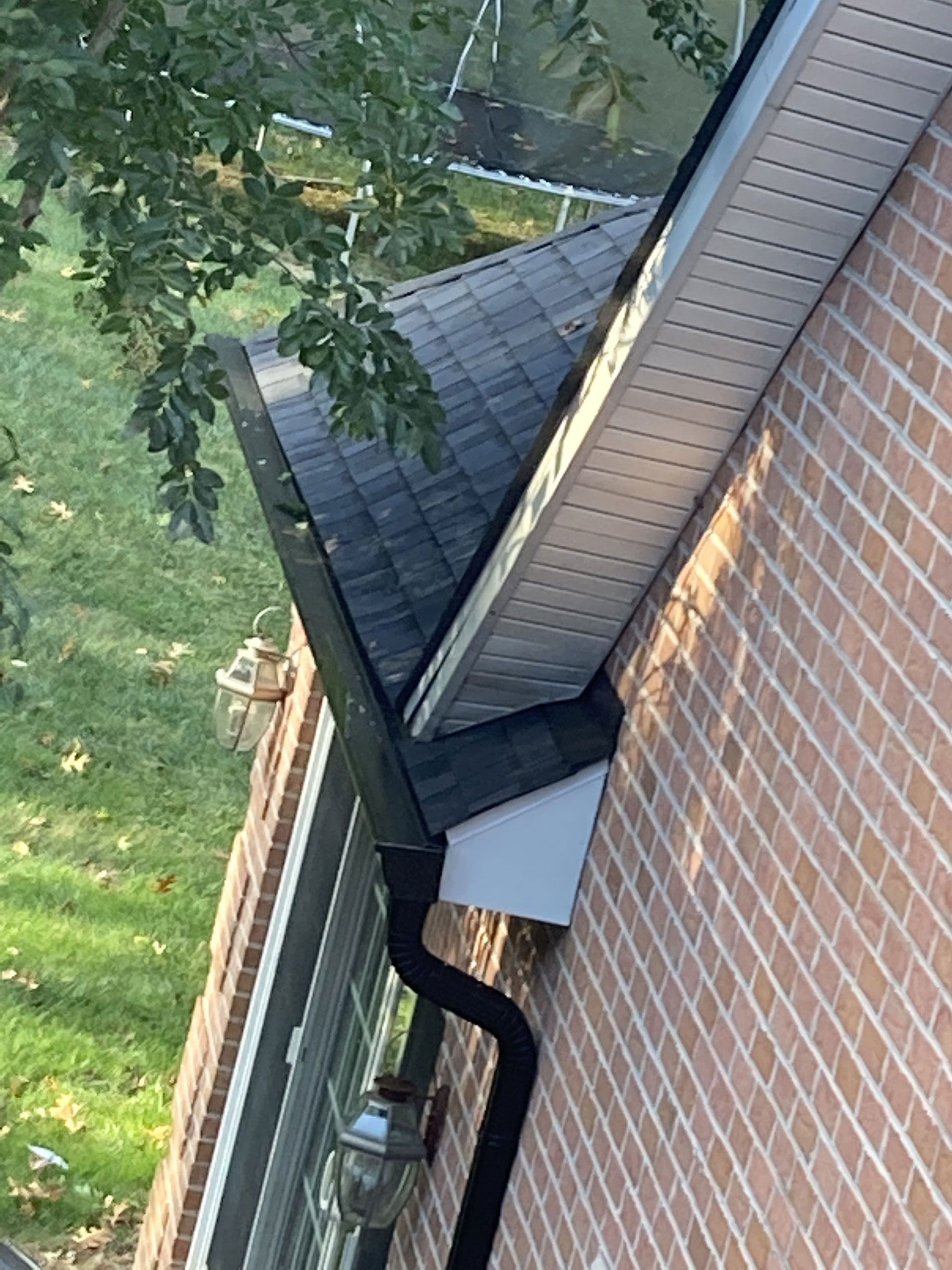 Brick building corner with dark roof, black gutter, and white siding.