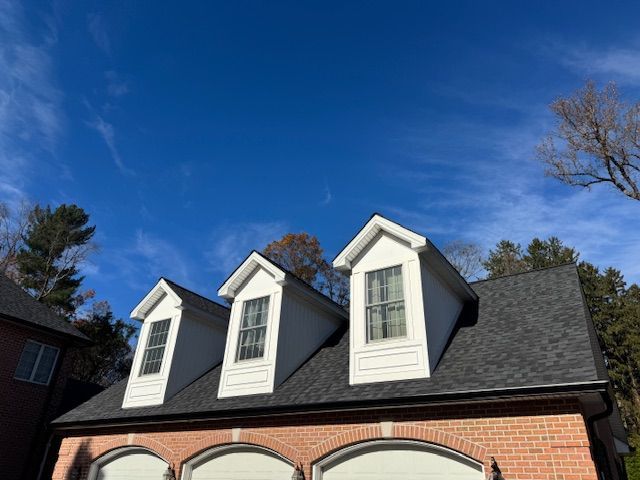 Three white dormers with windows on a brick building, set against a bright blue sky.