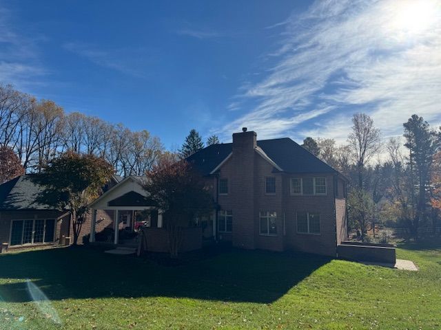 Two-story brick house with a dark roof and chimney, set against a blue sky with scattered clouds.