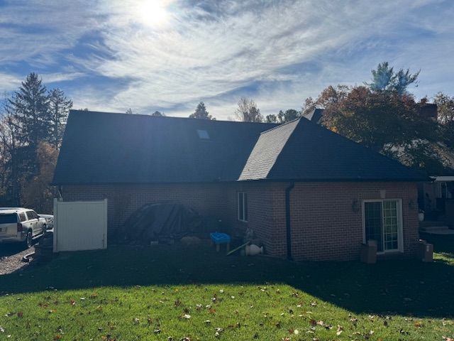 A brick house with a dark roof and a grassy lawn under a partly cloudy sky.