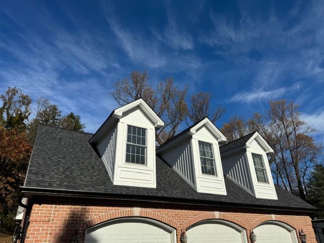 Brick building with three garage doors and dormers under a blue sky.
