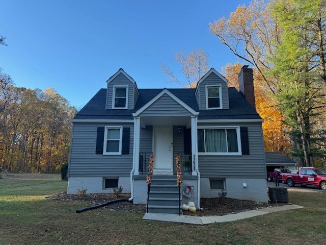 Gray house with black roof, two dormers, black shutters, and a front porch.