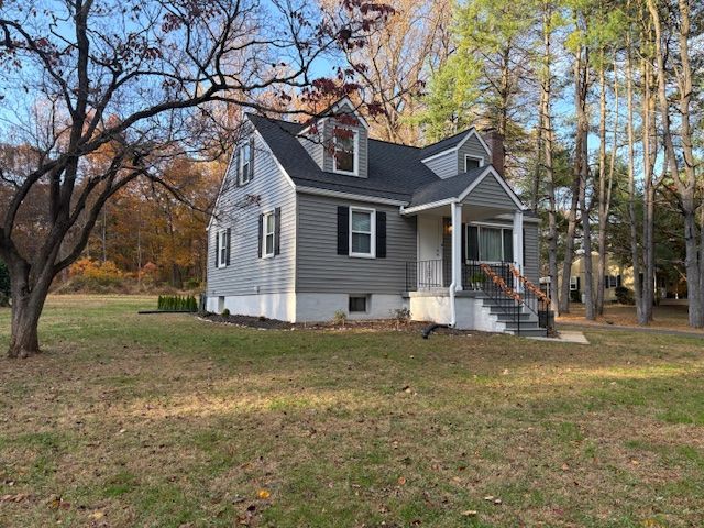 Gray and white house with black roof, small front porch, and dormers. Surrounded by trees and grass.