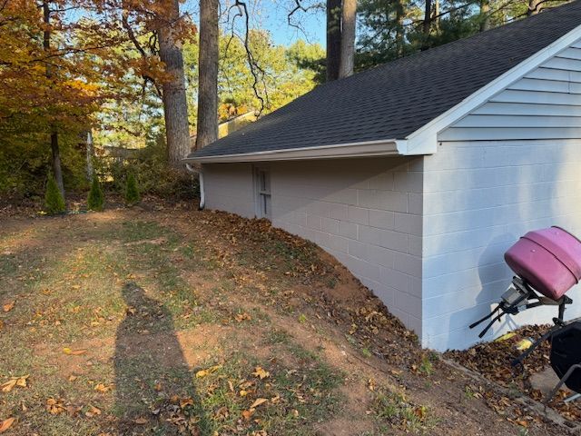 Side of beige building with dark roof, surrounded by fallen leaves and trees in an autumn setting.