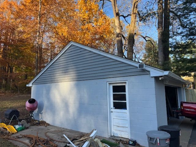 A detached garage with blue siding and a white door, surrounded by trees with fall foliage.