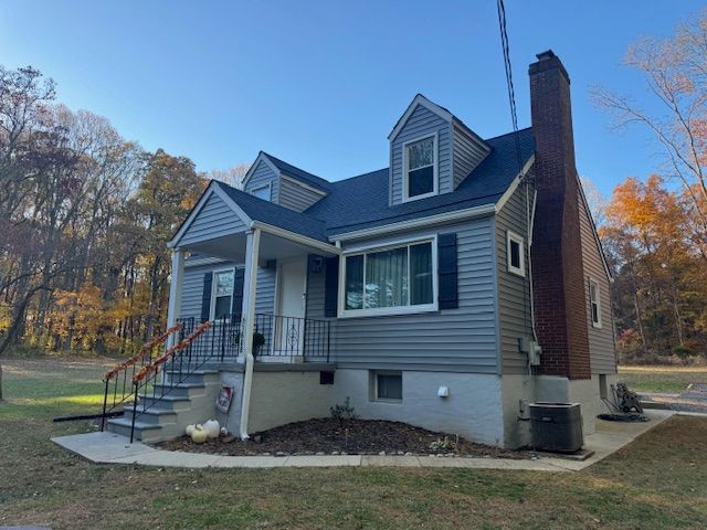 A gray house with a black roof, blue shutters, and a brick chimney on a grassy lot.