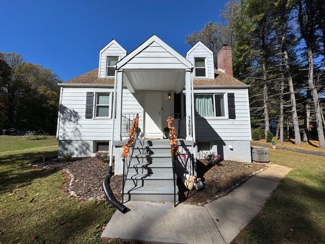 White house with a small porch, black shutters, and a concrete path. Sunny day with blue sky.