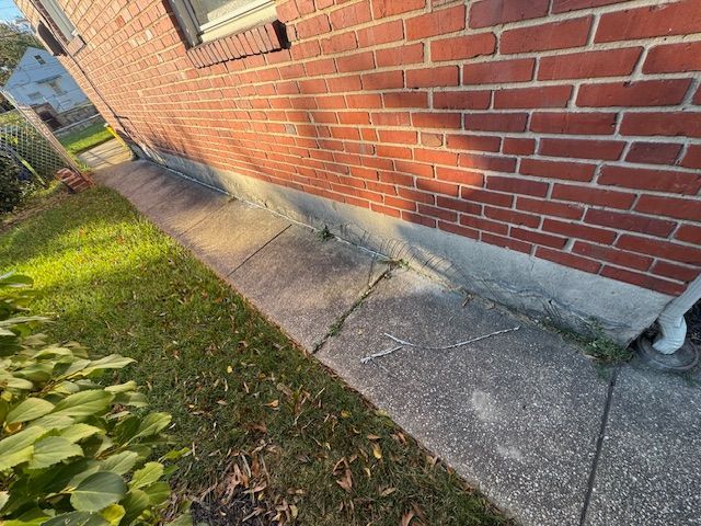 Brick building with a concrete walkway alongside. The walkway has cracks and some grass growing through.