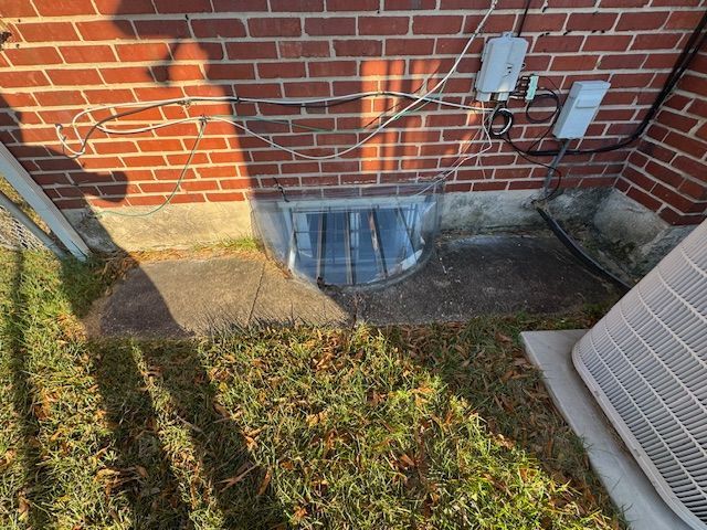Brick building exterior with a basement window well covered by a clear plastic cover.