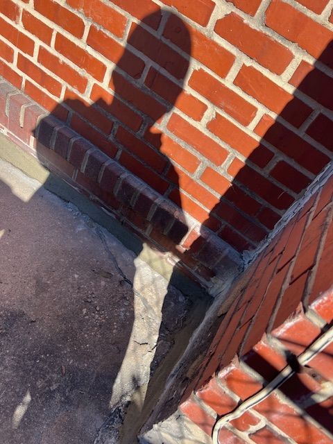 A person's shadow on a red brick wall, cast over a corner of a rooftop.